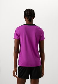 Short-sleeved, crew-neck shirt in bright purple with a black collar, worn with black shorts, featuring a smooth, moisture-wicking fabric.
