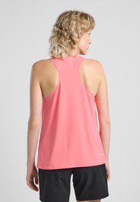 Top athletic senza maniche di colore rosa brillante, caratterizzato da un tessuto testurizzato e design a schiena a nuotatore. Abbinato a pantaloni corti scuri.