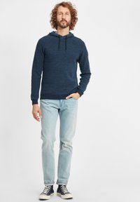 Marineblau strukturierter Hoodie mit einer frontalen Tasche, Kapuze mit Kordelzug und gerippten Bündchen, kombiniert mit hellblauen Jeans und Sneakern.
