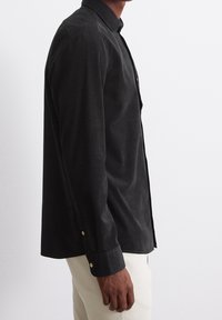 Camisa negra de manga larga en una tela suave y texturizada, con cuello abotonado y botones dorados en los puños.