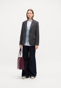 Blazer de cuadros grises sobre un chaleco azul claro, camisa blanca, jeans oscuros de pierna ancha, zapatos plateados y una bolsa tote color burdeos.