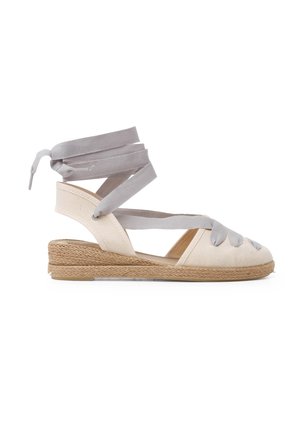 Espadrillesandal med en beige kanvasoverdel, grå båndsnørrer og en sækryddet kilehælt. Åben tå-design med krydsdetaljer.