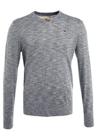 Šedý pletený svetr s designem do V, dlouhými rukávy a jemně strukturovaným povrchem. Na hrudi má malou logovku.