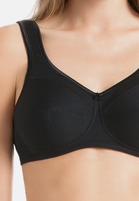 Schwarzer BH mit breiten Trägern, V-Ausschnitt und Nahtdetails an den Cups. Hergestellt aus glattem Stoff mit einer subtilen Textur.