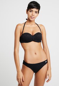 Melnā bikini komplekts, kas sastāv no teksturēta bandeau augšdaļas ar halter jostām un atbilstošām zemu jostasvietu apakšdaļām, abām ar ģeometrisku rakstu.