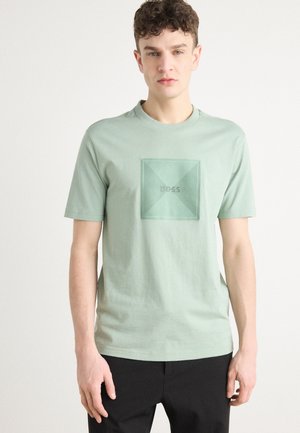 Camiseta de manga corta verde claro de algodón, con un diseño cuadrado texturizado que lleva el texto "BOSS" en el centro. Ajuste casual.