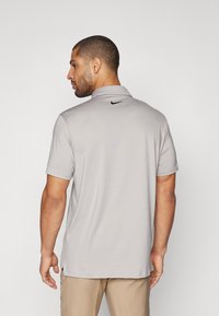 Gaiši pelēks polo krekls ar apkakles izgriezumu un īsām piedurknēm. Aizmugurē pie apkakles ir melns Nike logo. Mīksta auduma tekstūra.