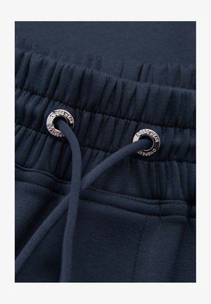 Elastic navyblåt taljebånd med snor og metaløjer indgraveret med "OMBREE WEAR" på mørkt stof.