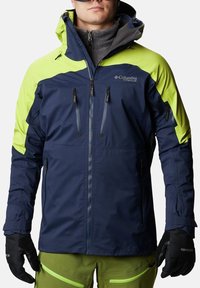 Giacca impermeabile blu navy e verde brillante con chiusura a zip, numerose tasche con zip e cappuccio regolabile. Tessuto testurizzato per il calore.