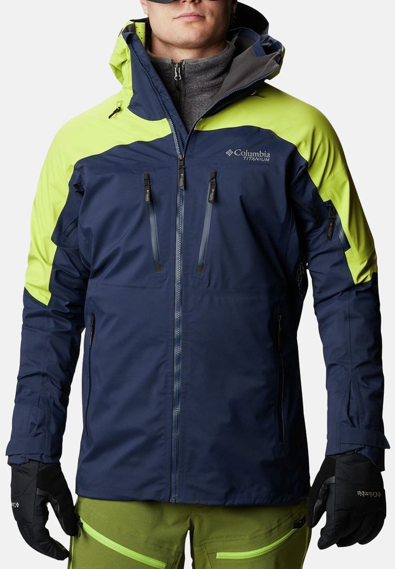 Giacca impermeabile blu navy e verde brillante con chiusura a zip, numerose tasche con zip e cappuccio regolabile. Tessuto testurizzato per il calore.