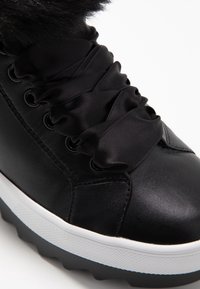 Baskets en cuir noir avec semelle blanche épaisse, larges lacets noirs en satin et bordure en fourrure autour de la cheville.