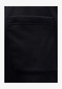 Tela negra con superficie texturizada. Presenta un bolsillo visible con detalles cosidos, que muestra un material suave y duradero.