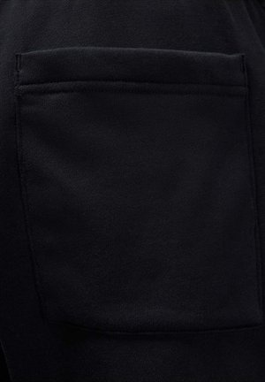 Tela negra con superficie texturizada. Presenta un bolsillo visible con detalles cosidos, que muestra un material suave y duradero.