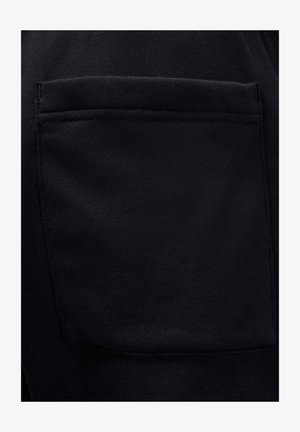 Zwarte stof met een gestructureerd oppervlak. Voorzien van een zichtbare zak met gestikte accenten, die een glad, duurzaam materiaal toont.