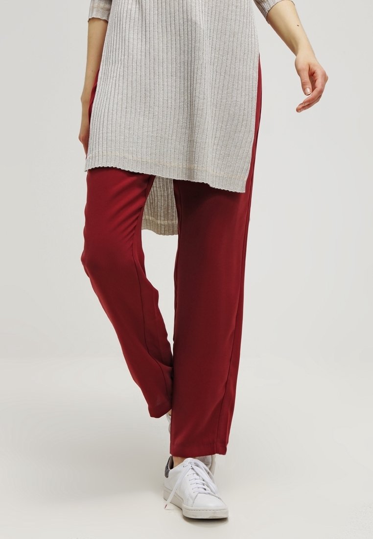 Red, loose-fitting pants made of lightweight fabric, paired with a long, light gray ribbed tunic and white sneakers. Smooth texture and casual design.