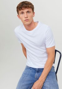 T-shirt blanche à manches courtes en coton, avec un col rond et une texture lisse, associée à un jean en denim bleu clair.