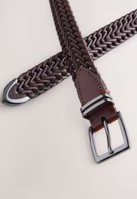 Ceinture en cuir marron tressé avec boucle élégante en métal argenté. Présente une texture lisse et une surpiqûre accentuée à l'extrémité en cuir.