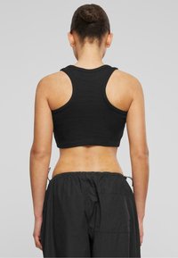 Must mustriga mustriga tank top laiemate õlgade rihmadega, sobiv vorm ja ribikoes, kombineeritud vabade mustade nööriga pükstega.
