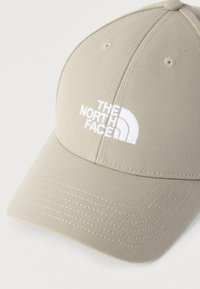 Μπεζ καπέλο κατασκευασμένο από ύφασμα, με καμπυλωτό γείσο, σχεδιασμό με έξι πάνελ και κεντημένο λευκό λογότυπο "The North Face." Διακρίνονται λεπτομέρειες ραφής.