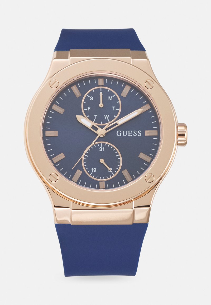 Reloj Guess con correa de silicona azul, caja de acero inoxidable dorado, esfera azul oscura, tres subesferas y marcadores de hora metálicos.