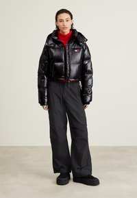 Chaqueta corta de plumas negra con acabado brillante, capucha desmontable, diseño acolchado, combinada con pantalones negros de corte holgado y zapatos de plataforma.