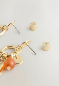 Gold-tone earrings featuring a large circular hoop, a smooth orange bead, and small circular accents, alongside two earring backs.
