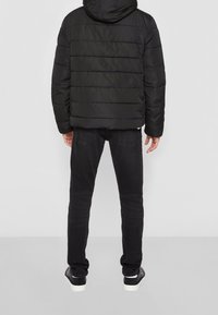 Svart puffjacka med horisontellt quiltat mönster, huva och långa ärmar. Matcher med svarta jeans och svarta sneakers med vita sulor.