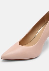 Escarpin en cuir rose avec un bout pointu et un design découpé sur le dessus. Texture lisse avec un léger éclat et un talon élancé.