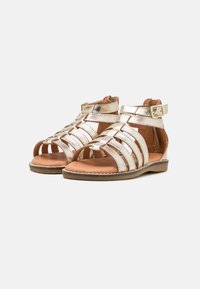 Metallisch goldene Riemchensandalen mit offenen Zehen, flacher Sohle, Knöchelriemen mit Schnalle und einem geflochtenen Design. Strukturiertes Leder-Finish.