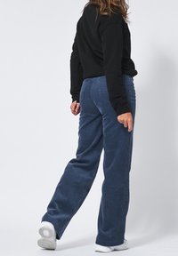 Siniset corduroy-housut, joissa on suora lahkeiden malli. Ominaisuuksiin kuuluu uritettu pinta ja takataskut. Yhdistetty mustan neuleen ja valkoisten sneakers-kengien kanssa.