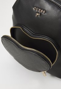 Sac à dos en simili cuir noir avec quincaillerie dorée, doté d'une poche avant zippée et d'un motif en relief de losanges sur la poche.