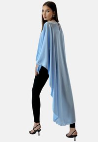 Ljust blå satinmantel med långa ärmar och hög-låg nederkant, kombinerad med svarta leggings och svarta klackar med remmar. Bakpartiet har en nyckelhålsdetalj.