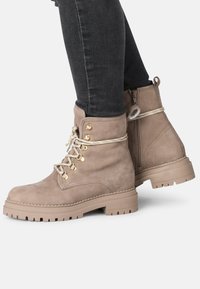 Bottines en suède beige avec une semelle épaisse, bout rond, œillets dorés et lacets beiges, dotées d'une fermeture éclair sur le côté pour un enfilage facile.