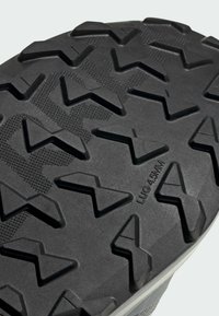 Suela de zapato de goma negra con un patrón de huella en zigzag profundo. Presenta lugs elevados con una superficie texturizada para mayor agarre. Marcada "LUG 4.5MM."
