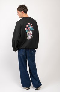 Zwart oversized sweatshirt met een kleurrijke bloemenvaasprint op de achterkant. Gepaard met losse blauwe denim broek.