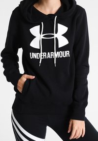 Czarna bluza z kapturem wykonana z miękkiego materiału, z dużym białym logo Under Armour i sznurkami, z przednią kieszenią i ściągaczami na rękawach.