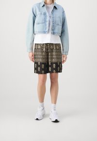 Světle modrá denimová zkrácená bunda, bílý tričko, černé šortky se zlatým listovým potiskem a bílé tenisky s šedými akcenty.