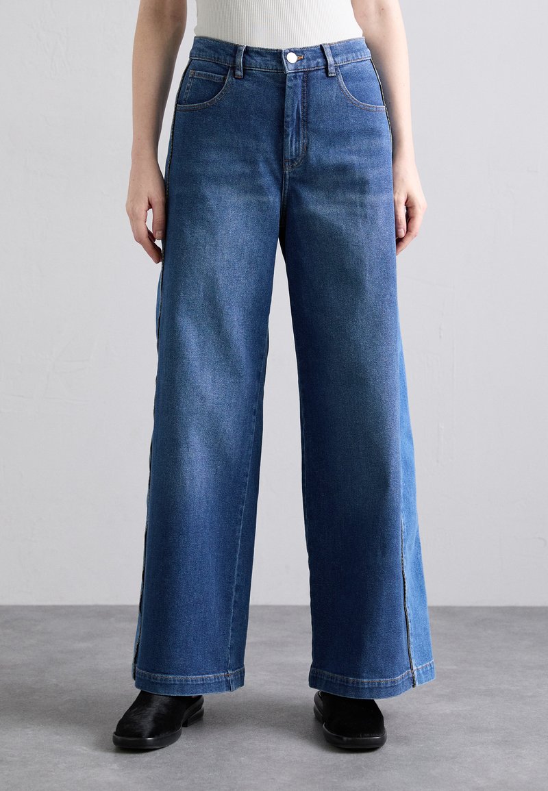 Blaue Denim-Jeans mit weitem Bein und hoher Taille, ausgestattet mit Fronttaschen, einem Knopfverschluss und einem leichten Ausbleichen des Stoffes.