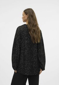 Pull noir à coupe ample, orné de reflets métalliques, avec des manches longues et un ourlet arrondi. Le tissu texturé ajoute un intérêt visuel.