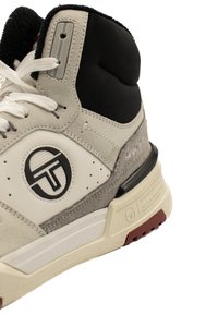 Hög sneaker i ljusgrå mocka och läder, med svarta accenter. Har en cirkulär logotyp och en distinkt texturerad sula. Snörningsdesign och vadderad krage.