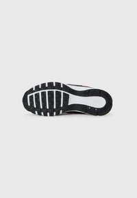 Melnas un baltas Nike skriešanas apavu gumijas zole ar redzamām protektora struktūrām un mazām saķeres knopkām.