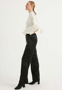 Crème gebreide trui met lange mouwen, gecombineerd met zwarte satijnen joggers met een elastische tailleband en drawstring. Zwarte enkellaarzen met een hak.