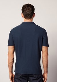 Marinblå pikétröja med korta ärmar och platt krage. Tillverkad av texturerat tyg, med rak nederkant och minimalistisk design.