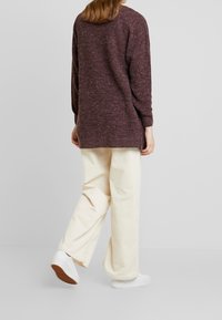 Lila teksturoitu villapaita, pitkät hihat, yhdistettynä vaaleisiin corduroy-latvasukkiin ja valkoisiin lenkkareihin. Asu on rento ja mukava.