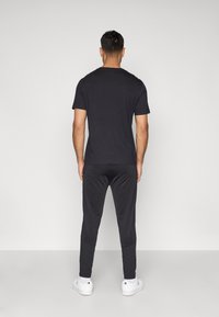 Schwarzes Kurzarm-T-Shirt kombiniert mit enganpassenden dunklen Hosen. Das Outfit zeichnet sich durch eine glatte Textur und ein lässiges, minimalistisches Design aus.