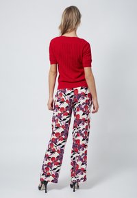 Suéter corto de manga corta con nervios rojos, combinado con pantalones de pierna ancha florales en blanco, rojo y púrpura, que presentan una textura suave y un ajuste relajado.