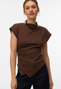 Haut marron à manches courtes avec un design drapé et un ourlet asymétrique. Le tissu a une texture lisse, associé à un collier de perles noires.