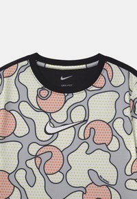 Kortärmad Nike Dri-FIT t-shirt med abstrakta svart-outline-former fyllda med gröna och orange prickar på en ljusgrå bakgrund.