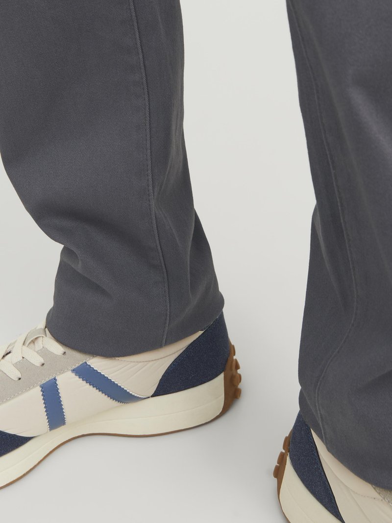 Dunkelgraue Hose mit entspannter Passform, kombiniert mit Sneakers im Retro-Stil, die ein beigefarbenes Obermaterial, marineblaue Akzente und eine strukturierte Sohle aufweisen.