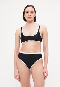 Črn bikini komplet z zgornjim delom s kvadratnim izrezom in belim obrobom ter ujemajočimi visoko pasnimi hlačkami. Gladka tekstura z minimalno kovinsko opremo.